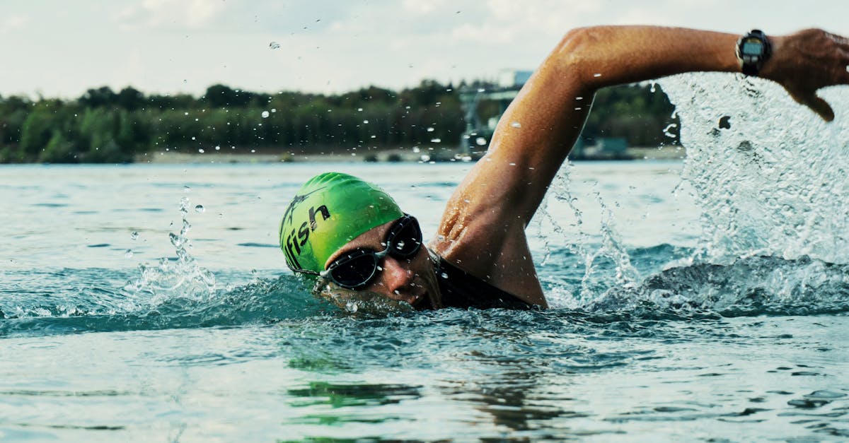 A male swimmer in a green cap and goggles competing in an open water race. The repetitive strain of swimming can result in scar tissue formation in the rotator cuff