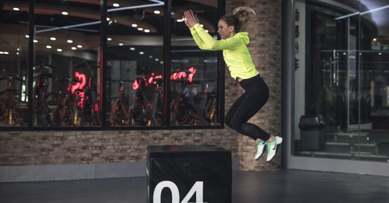 Fit young woman in sports wear executing a box jump indoors, promoting fitness and health in a modern urban gym. Ballistic training exercises, chiropractic exercise coach.