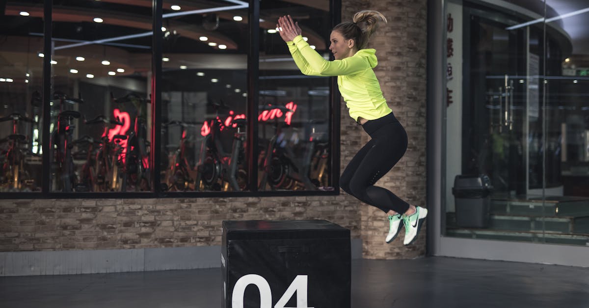 Fit young woman in sports wear executing a box jump indoors, promoting fitness and health in a modern urban gym. Ballistic training exercises, chiropractic exercise coach.