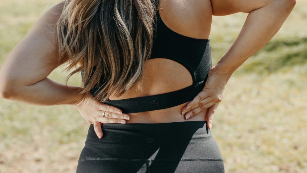 Close-up of a woman holding her back, suggesting low back pain outdoors.