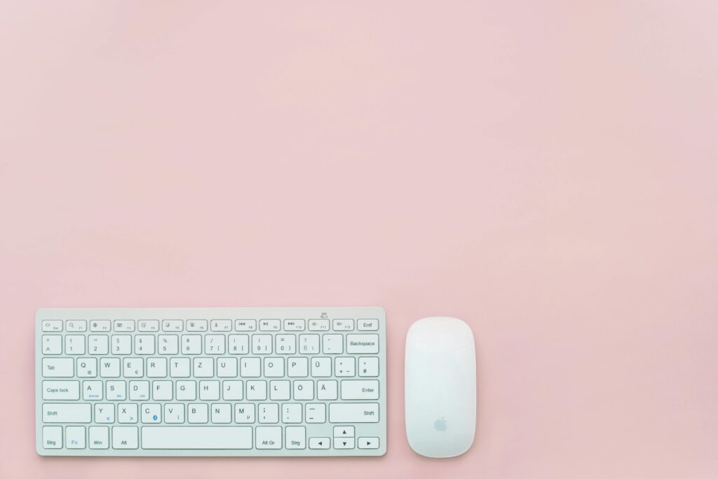 A clean and minimalist flat lay of a white keyboard and mouse on a pastel pink background. Perfect for feminine office themes.