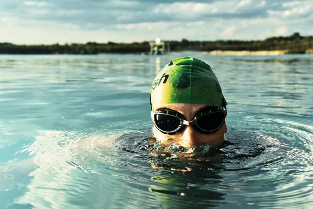 A determined swimmer in goggles and cap emerges from a tranquil lake on a sunny day. Scar Tissue development around the rotator cuff is a common repetitive strain injury associated with swimming.