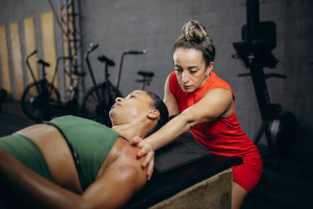 A therapist assists a woman with manual therapy (Active Release Technique) to improve flexibility and mobility in a gym environment.