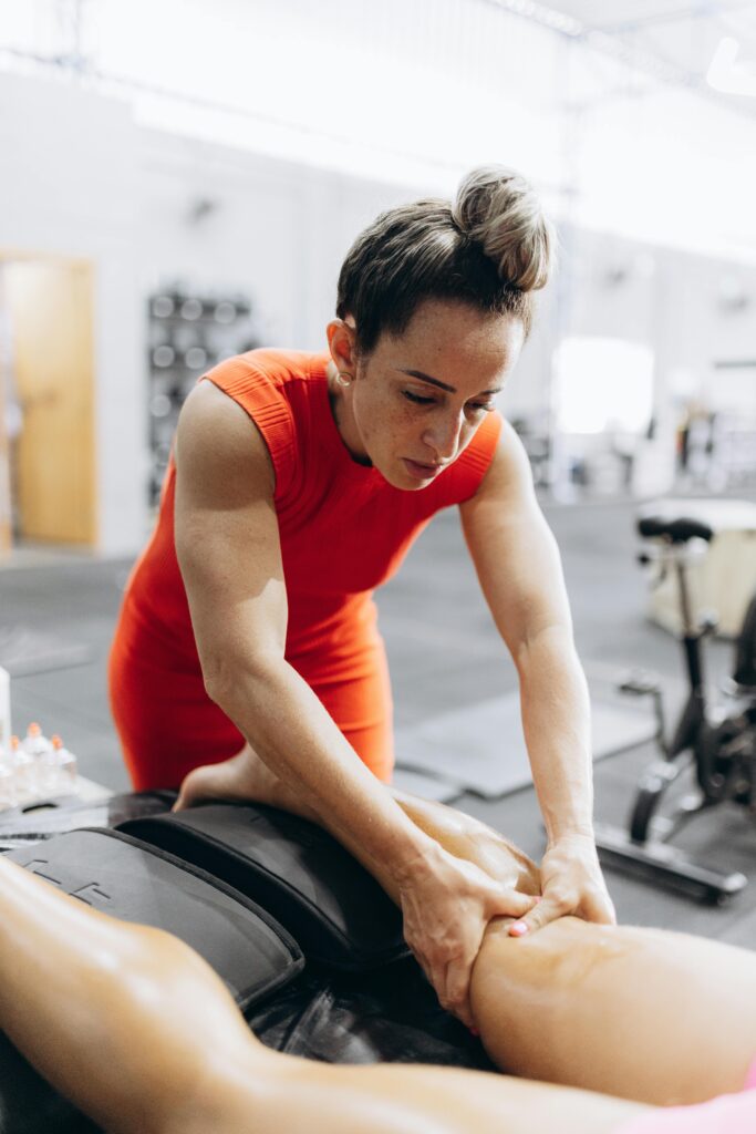 A therapist in red performs Active Release Technique on a client in a gym setting, enhancing recovery.