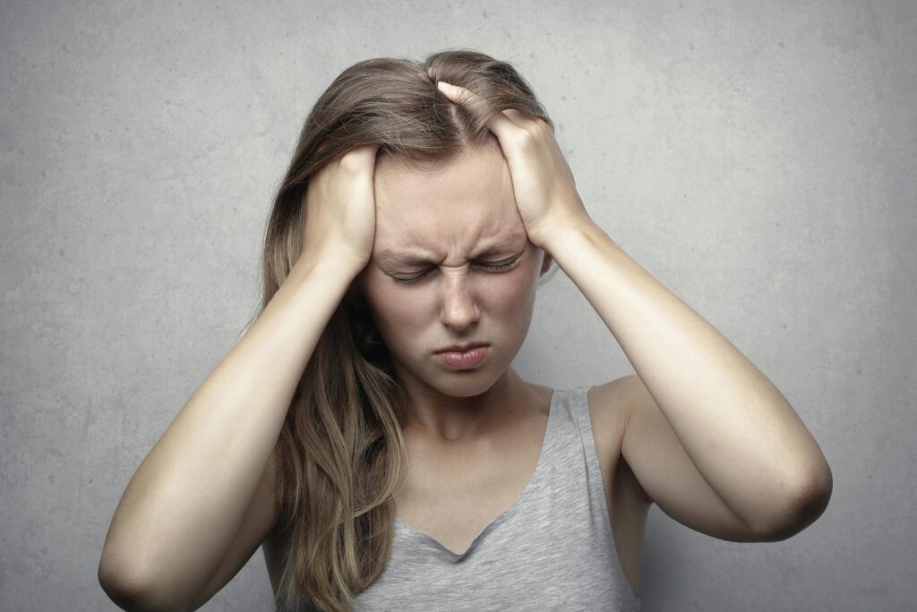 Young woman expressing stress and frustration while holding her head with a headache. Management can be chiropractic for headaches.