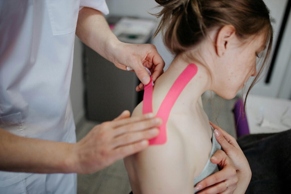 A chiropractor applies kinesio tape to a woman's shoulder for pain relief and treatment.