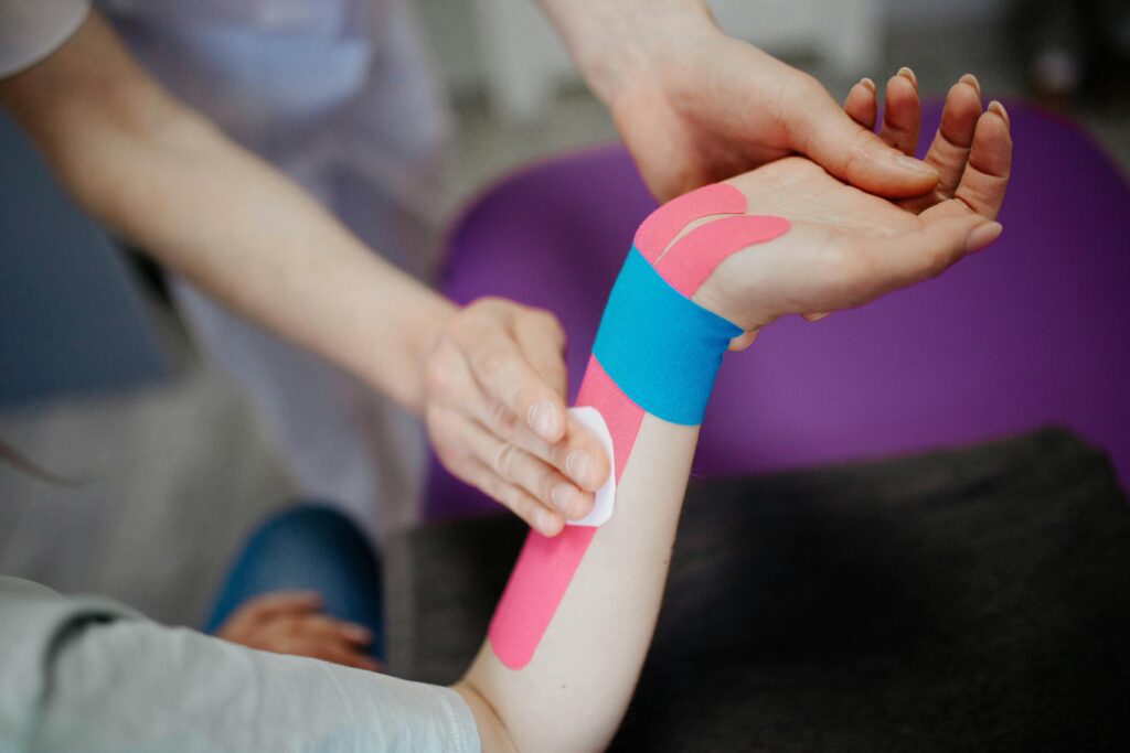 Close-up of kinesio tape application on a person's forearm by a therapist for therapeutic support.